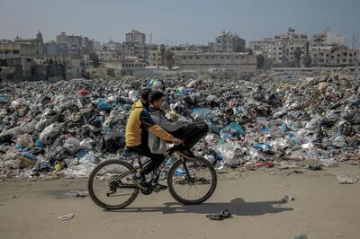 Palestinian boys pass on their bicycle a huge garbage dump along a main road in Gaza city on February 24, 2024. AFP