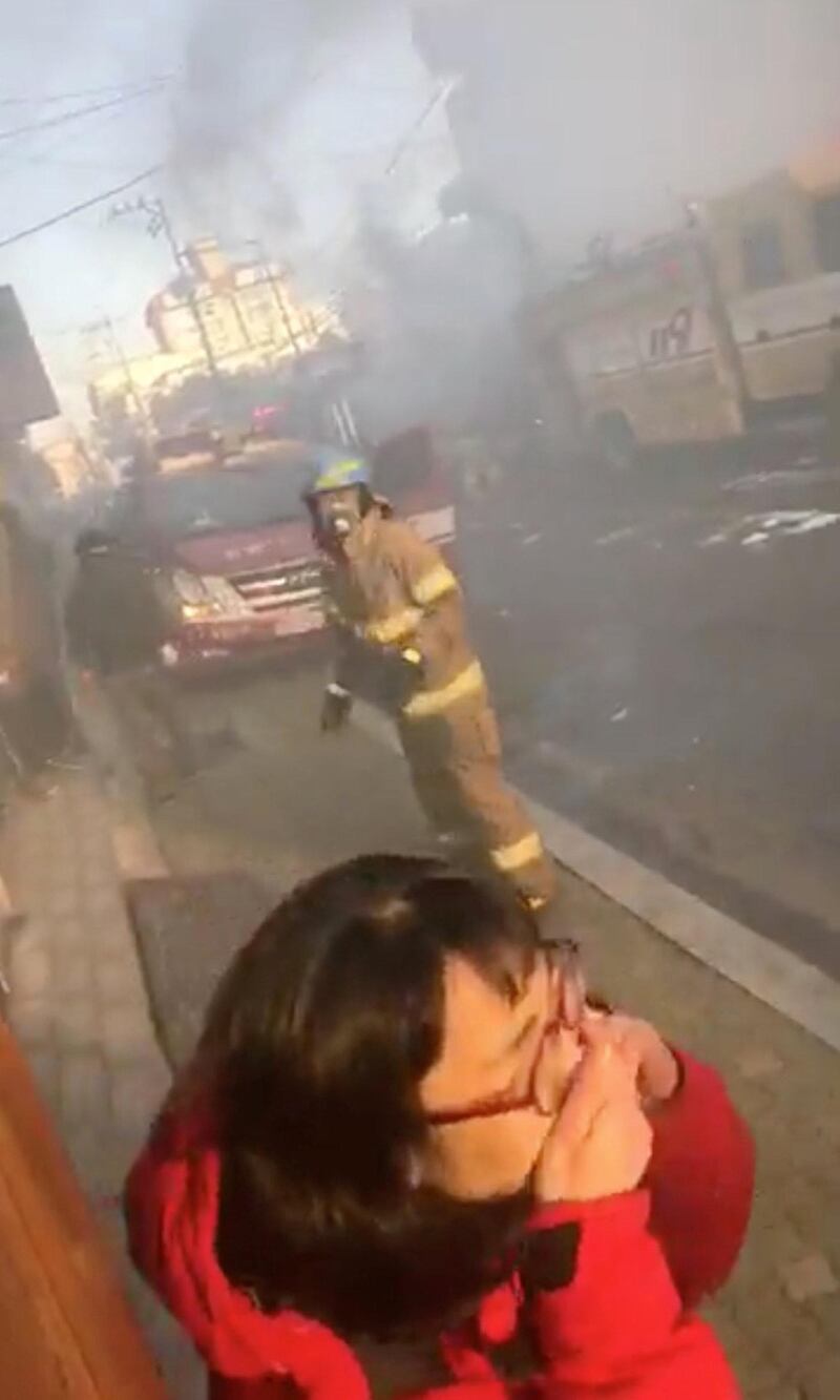 A woman covers her face from smoke.