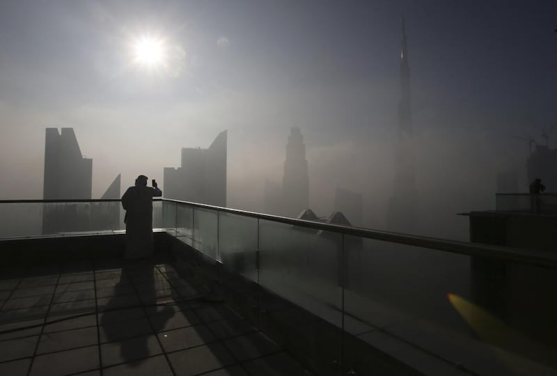 A man takes photos of the Burj Khalifa on a foggy day in Dubai. Flight disruptions continued at Dubai Airports due to a knock-on effect on scheduling. Kamran Jebreili / AP Photo
