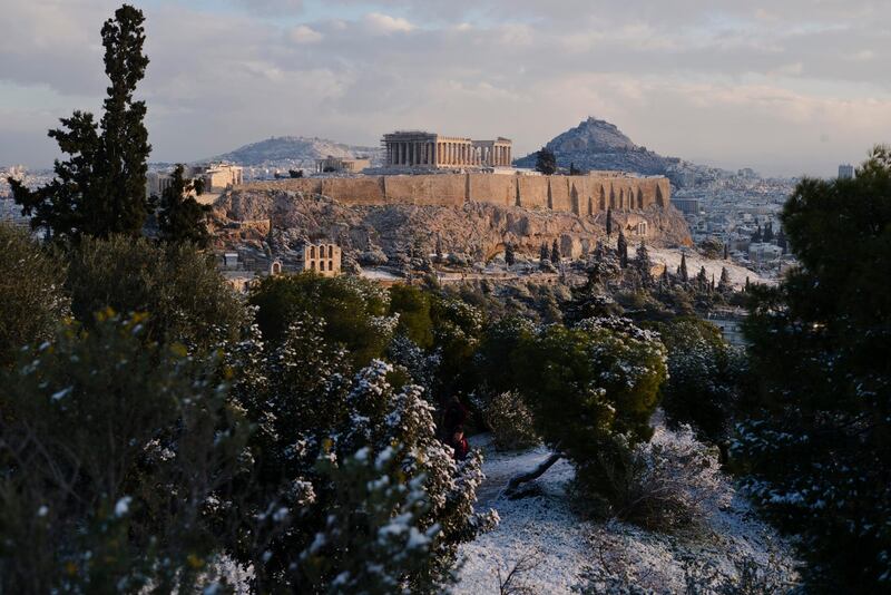 A man walks at Filopappos hill, with Acropolis hill in the background, after snowfall in Athens. AP Photo