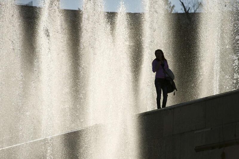 A woman walks by water fountains as she enjoys the warm weather in Paris. Alain Jocard / AFP Photo