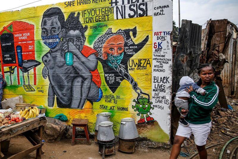 A woman carries a baby past an informational mural warning people about the dangers of the new coronavirus and how to prevent transmission, with words in Swahili reading, 'We are the Cure', painted by youth artists in Nairobi, Kenya. AP