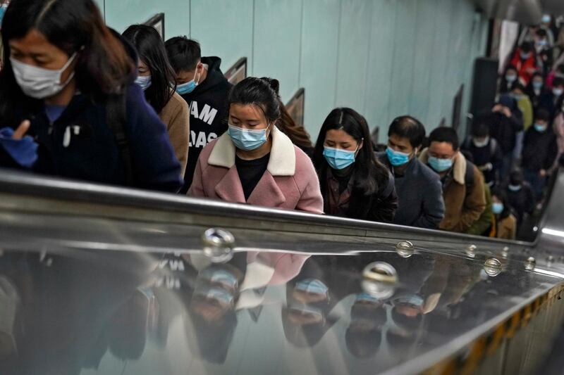 Commuters wearing face masks to help curb the spread of the coronavirus are reflected on a panels they ride an escalator at a subway station during the morning rush hour in Beijing. AP Photo