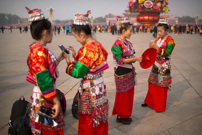 Women in traditional dress check their smartphones in Tiananmen Square in Beijing. Mark Schiefelbein / AP Photo