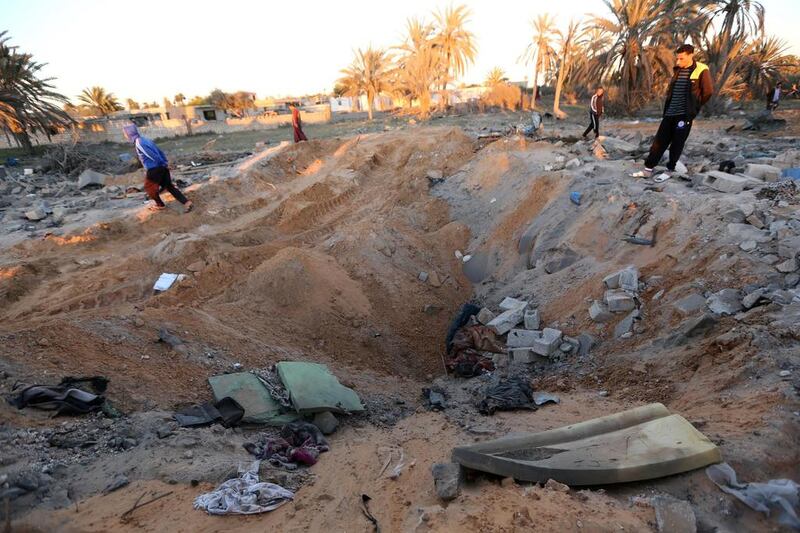 Libyans stand next to a crater and debris at the site of a jihadist training camp, targeted in a US air strike, near the Libyan city of Sabratha. (AFP / MAHMUD TURKIA)