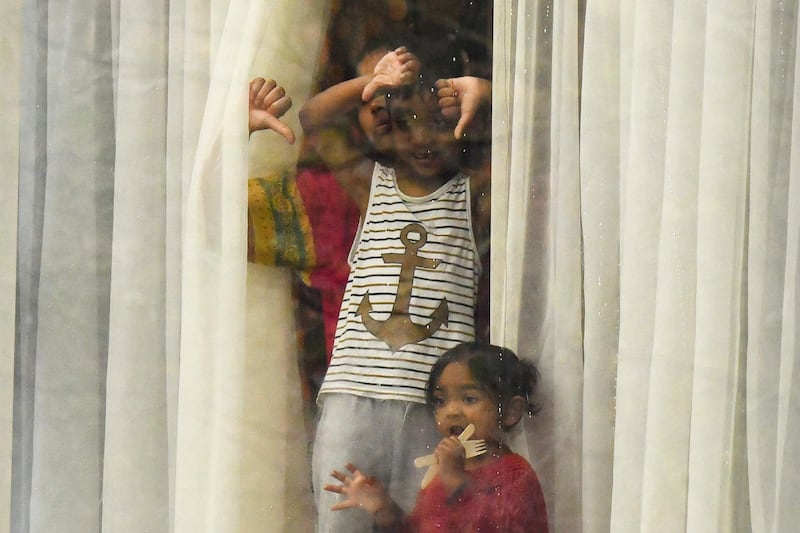 A woman accompanied by a boy and girl stand and gesture out of a window from inside the Radisson Blu hotel at Heathrow Airport in west London on February 17, 2021 where they are undertaking mandatory hotel quarantine because of the coronavirus pandemic. AFP