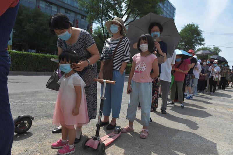 A woman adjusts a young girl's face mask as they wait in line. AFP