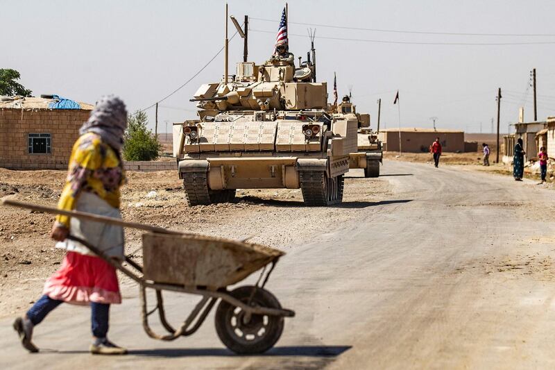 A woman pushing a wheelbarrow crosses the road as a patrol of US Bradley Fighting Vehicles approaches. AFP