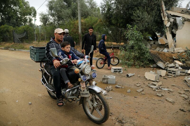 A Palestinian man and his son ride a motorcycle past the debris of a building destroyed in an Israeli air strike. Reuters