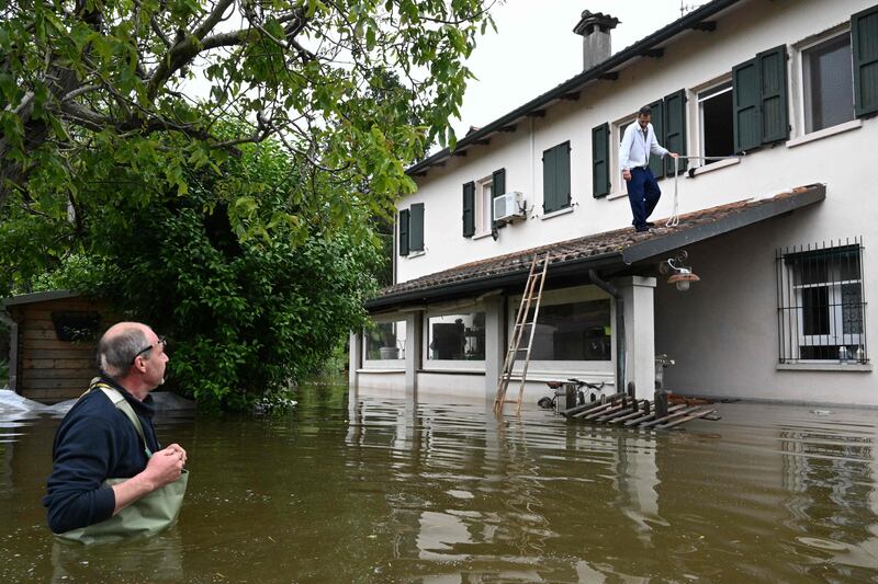 A man stranded in his flooded property uses a rope and a ladder to get out as his cousin looks on. AFP