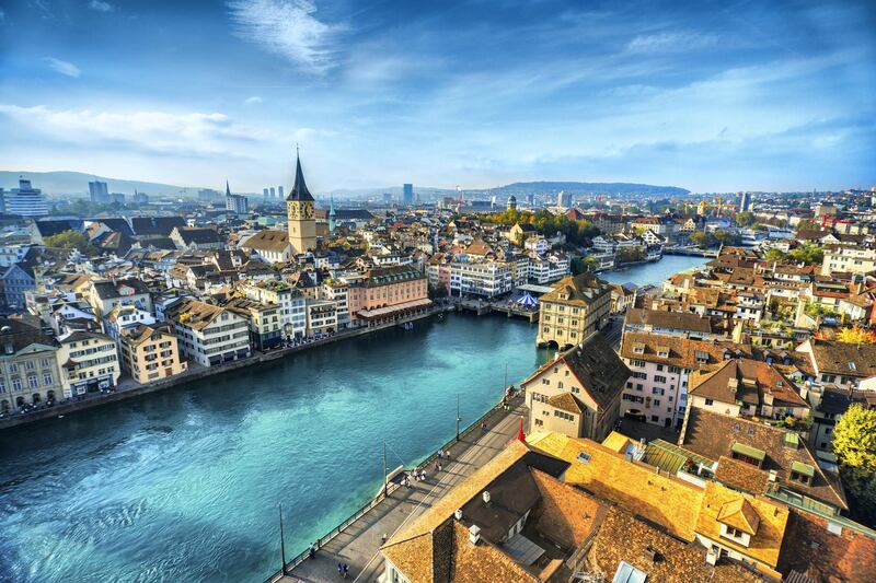 Aerial view of Zurich, Switzerland. Taken from a church tower overlooking the Limmat River. Beautiful blue sky with dramatic cloudscape over the city. Visible are many traditional Swiss houses, bridges and churches.