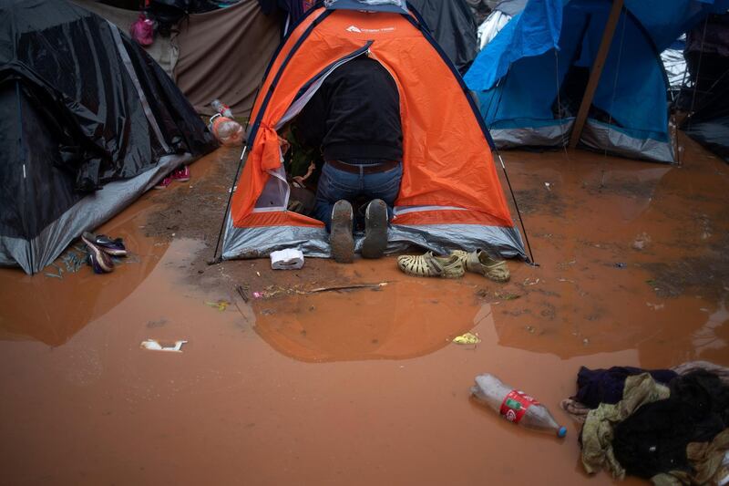 A migrant collects his belongings from his tent after rainfall. Reuters