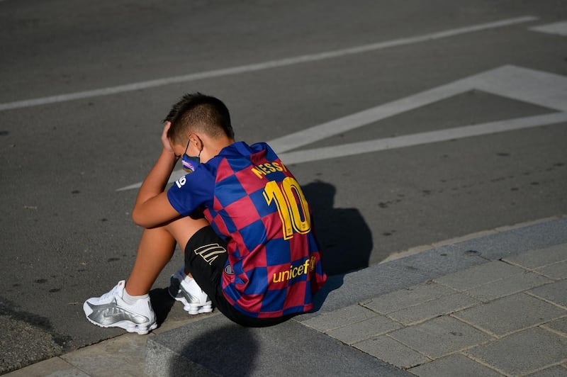 A boy sporting a Lionel Messi's shirt sits on the pavement outside the Barcelona's Ciutat Esportiva Joan Gamper in Sant Joan Despi waiting for the arrival of players to undergo a medical test for Covid-19. AFP