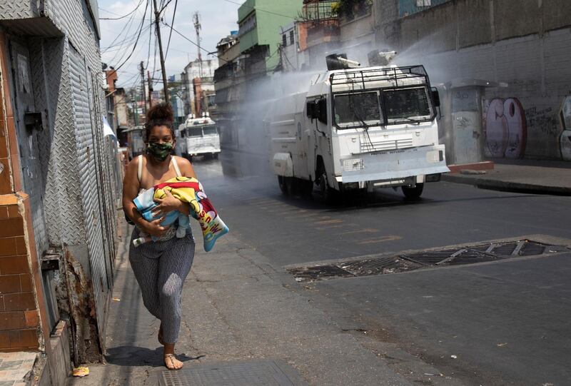 A woman carries her baby as the Bolivarian National Guard uses water cannon to disinfect the street. AP