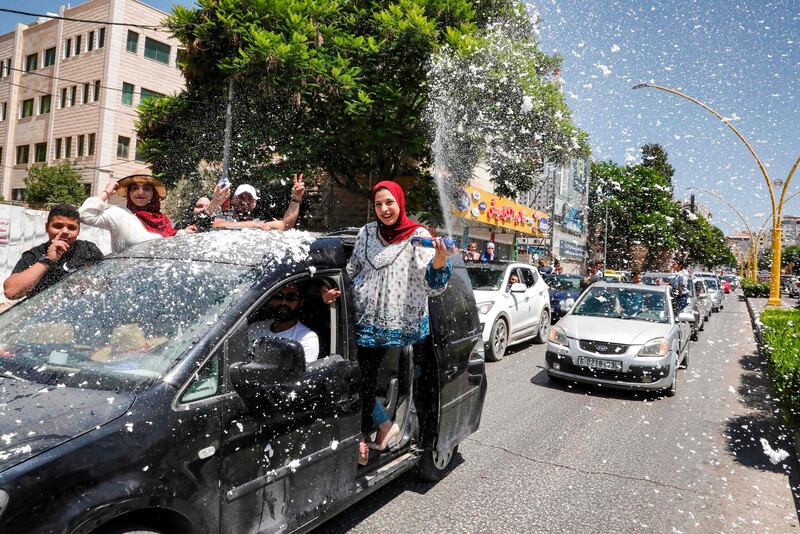 Palestinian high school students wave and spray artificial snow from a moving vehicle as they celebrate the announcement of their general secondary education examination (Tawjihee) results in a car procession.  AFP