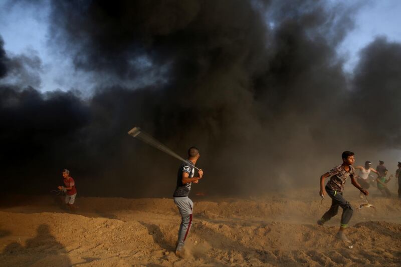 A protester hurls stones while others run after burn tires near the fence of the Gaza Strip border with Israel, during a protest east of Gaza City. AP Photo