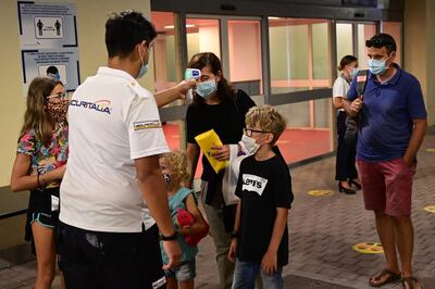 Passengers wearing protective mouth and nose masks have their temperature checked as part of the health security controls by a crew member as they board the MSC Grandiosa cruise ship prior to sailing from the northwestern port city of Genoa on August 16, 2020,  following the lifting of the lockdown several months ago to control the spread of the novel coronavirus, COVID-19, pandemic.   The first major cruise ship to set sail in the Mediterranean was poised to depart from Genoa as Italy's struggling travel industry hopes to regain ground after a bruising coronavirus hiatus, representing a high-stakes test for the global sector in the key Mediterranean market and beyond.  / AFP / Miguel MEDINA
