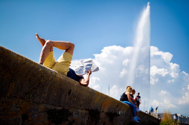 A man reads a newspaper as he enjoys the warm weather by the Geneva Water Fountain landmark, the so called 'Jet d'Eau' in French, on Lake Geneva, in Geneva, Switzerland. Valentin Flauraud / EPA