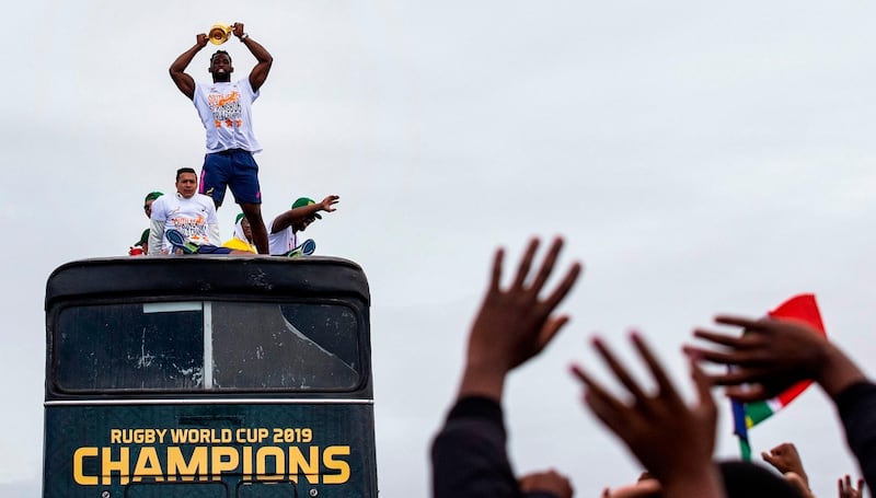 People cheer as South African Rugby captain Siya Kolisi (C) holds up the Web Ellis Trophy while the South African Rugby World Cup winner team parades on an open top bus through the streets of the city of Zwide , Port Elizabeth. AFP