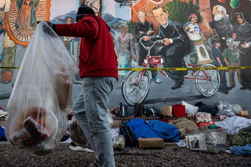 Immigrants clean up trash while others sleep outside a migrant shelter. Getty / AFP