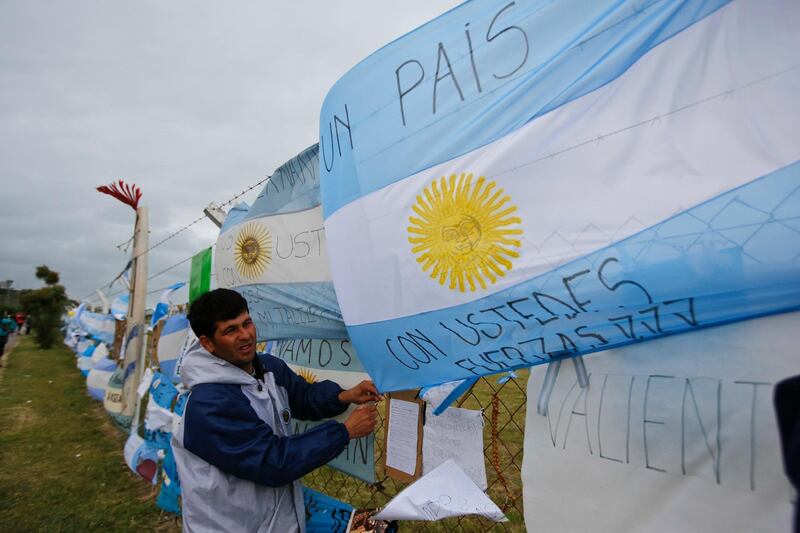 A man ties an Argentine flag carrying solidarity messages to a fence at the Mar de Plata Naval Base after the navy announced a sound detected during the search for the missing ARA San Juan submarine is consistent with that of an explosion, in Mar de Plata, Argentina, Thursday, Nov. 23, 2017. A Navy spokesperson said the search will continue until there is full certainty about the fate of thes ubmarine, adding there was no sign the explosion might be linked to any attack. (AP Photo/Esteban Felix)