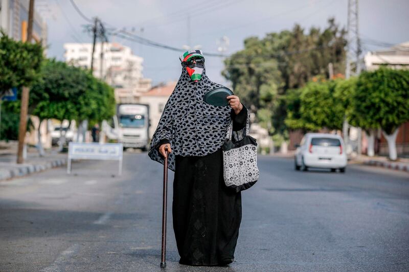 An elderly woman walks wearing a Palestinian flag as a face cover and a hat in the colours of the flag along a road in Gaza City, while on her way to withdraw her pension amidst a Covid-19  pandemic-imposed lockdown.  AFP