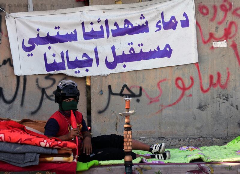 A protester smokes a shisha as he sits next to a banner reading in Arabic: 'The blood of our martyrs, will build the future of our generations' during a protest. EPA