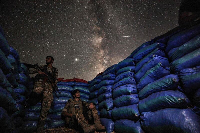 This long-exposure picture taken shows the Milky Way galaxy rising in the sky above Syrian fighters of the Turkish-backed National Front for Liberation group while on watch duty between sandbags in the town of Taftanaz along the frontlines in the country's rebel-held northwestern Idlib province.  AFP