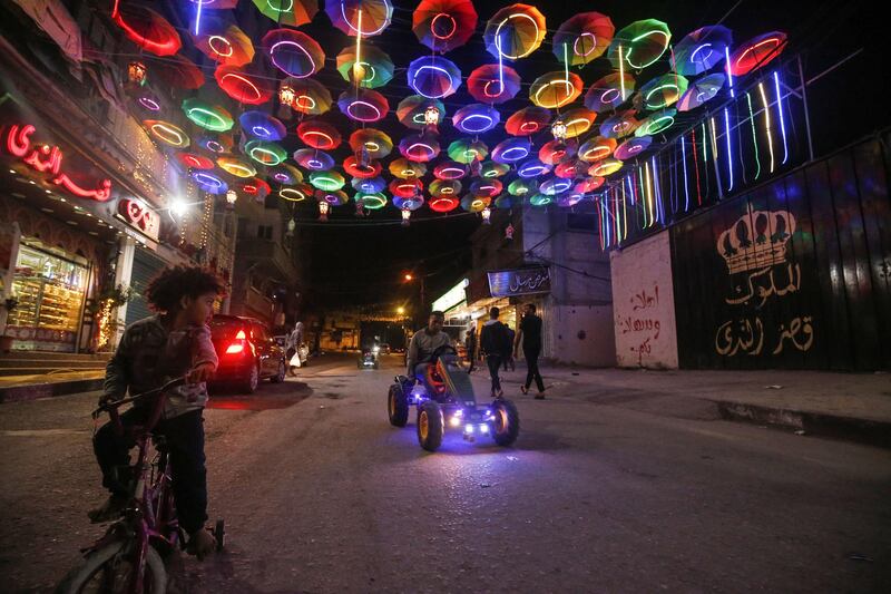 Young Palestinians ride a bicycle and a mini pedal-powered car along a street decorated with lit up umbrellas in Rafah in the southern Gaza Strip on the second night of the Muslim holy month of Ramadan early on April 25, 2020. (Photo by SAID KHATIB / AFP)