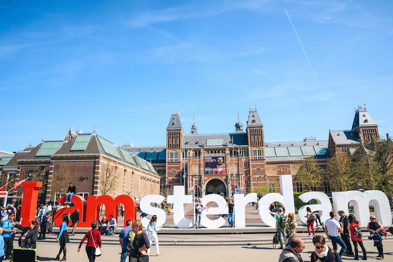 Amsterdam, Netherlands - April 18, 2018: Sign of 'I am Amsterdam' text sculpture with crowd of tourists in front of the Rijksmuseum on Museumplein in Amsterdam. The sculpture is part of the marketing campaign to promote tourism in in the city.