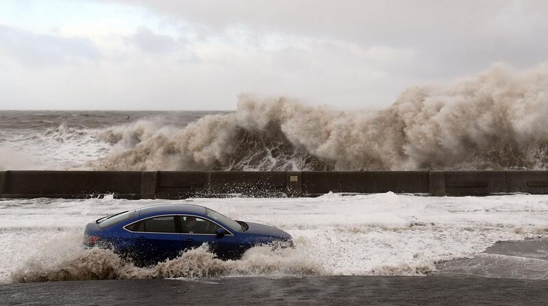 Waves crash over the tidal wall as a motorist travels along the coastal road in New Brighton, north west England.  Paul Ellis / AFP Photo