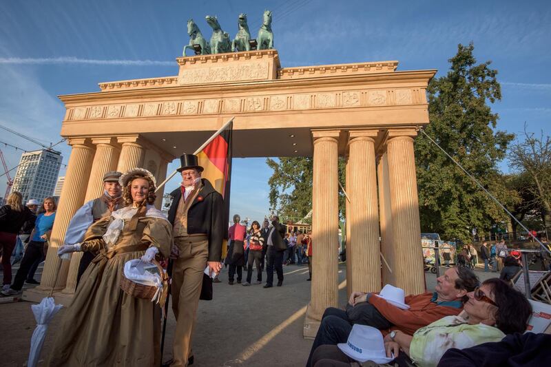 FRANKFURT AM MAIN, GERMANY - OCTOBER 03:  Elen Suchoroschenko (C), Fabio Begnotti (L) and Stefan Suchoroschenko (R) dressed in traditinell clothes of the 'Biedermeier' period of 1832 promote the 'Hambacher Castle' in front of a mock of the 'Brandenburger Tor' at the 25th anniversary citizens festival of German reunification on October 3, 2015 in Frankfurt, Germany. On October 3, 1990, following the end of the Cold War, western-oriented, capitalist and democratic West Germany and post-revolution, formerly communist East Germany reunited into a single state after 41 years of official separation. Though the integration of the two former states into one is seen by most as a success, differences remain, particularly in average incomes and pensions, which in eastern Germany are lower.  (Photo by Thomas Lohnes/Getty Images)