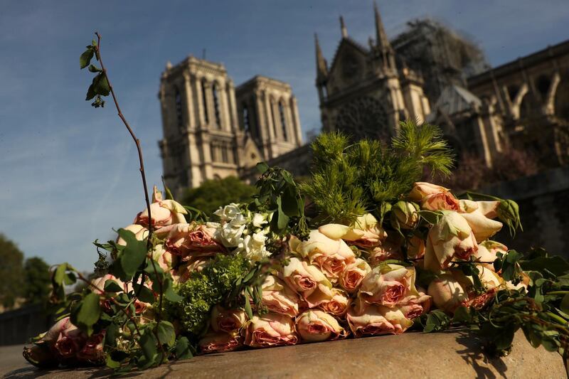 A bunch of flowers lies by the Seine riverside near the Notre Dame cathedral, background, in Paris, Thursday, April 18, 2019. France is paying a daylong tribute Thursday to the Paris firefighters who saved the internationally revered Notre Dame Cathedral from collapse and rescued its treasures from encroaching flames. (AP Photo/Francisco Seco)