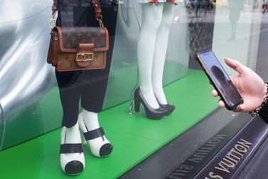 A pedestrian uses a smartphone beside women's clothing and handbag in the window display of a Louis Vuitton luxury goods store in Paris, France, on April 14, 2021. Bloomberg