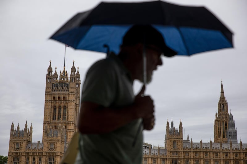 A pedestrian carrying an umbrella to shelter from the rain passes the Houses of Parliament in London, U.K., on Tuesday, June 30, 2020. U.K. Prime Minister Boris Johnson will commit to spending on infrastructure to rebuild the coronavirus-ravaged U.K. economy in a major policy speech Tuesday and say that balancing the books must wait until recovery is secure. Photographer: Simon Dawson/Bloomberg