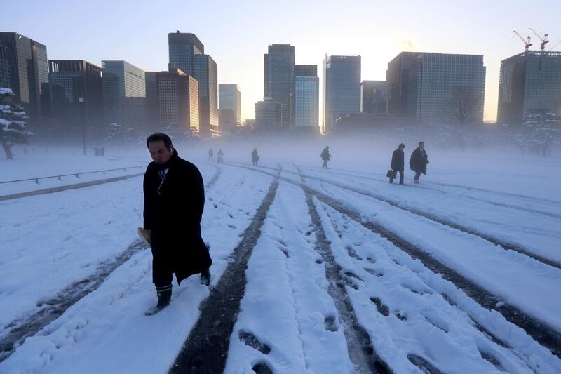 Morning commuters walk across a snow-covered field on the grounds of the Imperial Palace as buildings stand in the business district in Tokyo on Tuesday, Jan. 23, 2018. Takaaki Iwabu / Bloomberg
