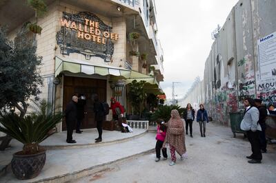 FILE - In this Friday, March 3, 2017 file photo, People pass by the "The Walled Off Hotel" and the Israeli security barrier in Bethlehem. In Jesus' traditional birthplace, some say the protests that erupted over President Donald Trumpâ€™s recognition of contested Jerusalem as Israel's capital have hurt their holiday business. (AP Photo/Dusan Vranic, File)