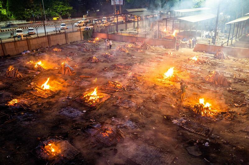 TOPSHOT - Men are seen around the burning pyres of victims who lost their lives due to the Covid-19 coronavirus at a cremation ground in New Delhi on April 26, 2021. / AFP / Jewel SAMAD
