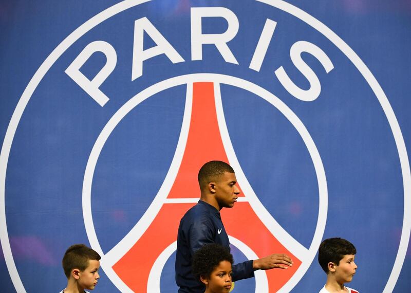 Paris Saint-Germain's French forward Kylian Mbappe and children walk in front of a Paris Saint-Germain logo. AFP