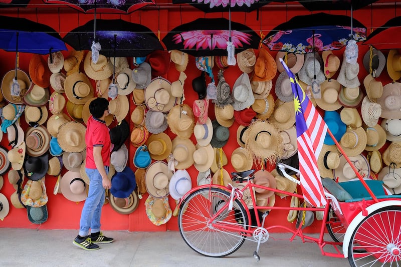A person stands in front of a hat and umbrella stall in Kuala Lumpur, Malaysia. Bloomberg