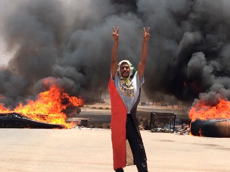 A protester flashes the victory sign in front of burning tires and debris on road 60, near Khartoum's army headquarters, in Khartoum, Sudan. AP Photo