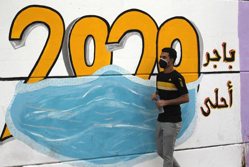 A mask-clad Iraqi man walks past a mural painting showing the digits 2020 covered by a face mask worn around the world as a means of protection against the coronavirus,  in the capital Baghdad's central Tahrir Square, on October 1, 2020. - Thousands of Iraqis gathered today in the capital Baghdad and in the country's south on the first anniversary of the start of unprecedented protests demanding the fall of the ruling class. (Photo by AHMAD AL-RUBAYE / AFP)