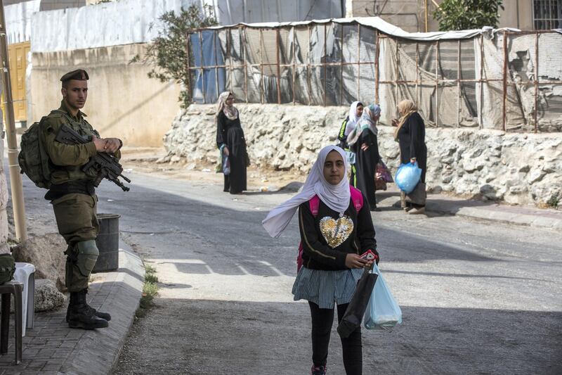 An Israeli soldier stands watch as Palestinian women and school children return home in the Palestinian Tel Rumeida neighborhood. Three other Hebron enclaves houses 800 illegal settlers who live among its 200,000 Palestinians.Hebron . The Israeli army and government just opened a new archeological park nearby.(Photo by Heidi Levine for The National).