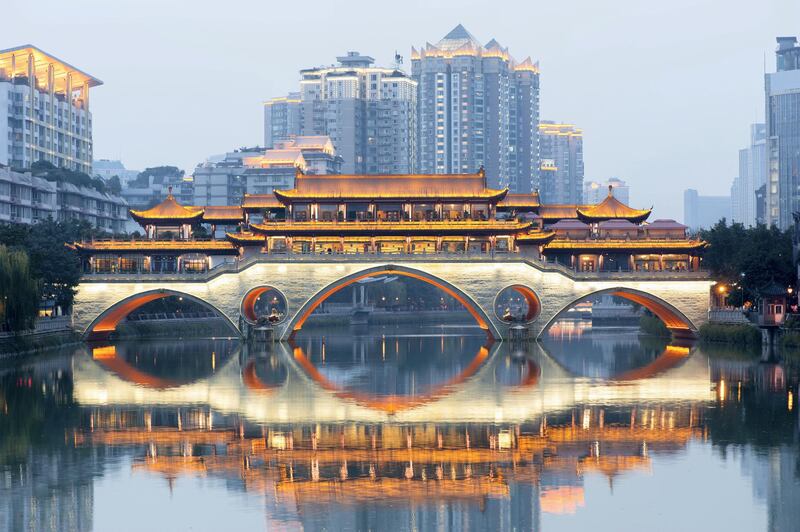 Anshun bridge with lights reflecting in the river at dawn with buildings in blue haze in the background, Chengdu, China