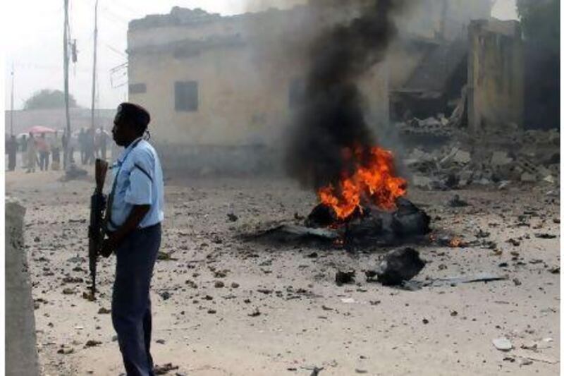 A policeman stands by the still-burning remains of a car shortly after it exploded in Mogadishu on December 6. Several people were killed when the explosives-laden vehicle was detonated. Farah Abdi Warsameh / AP Photo