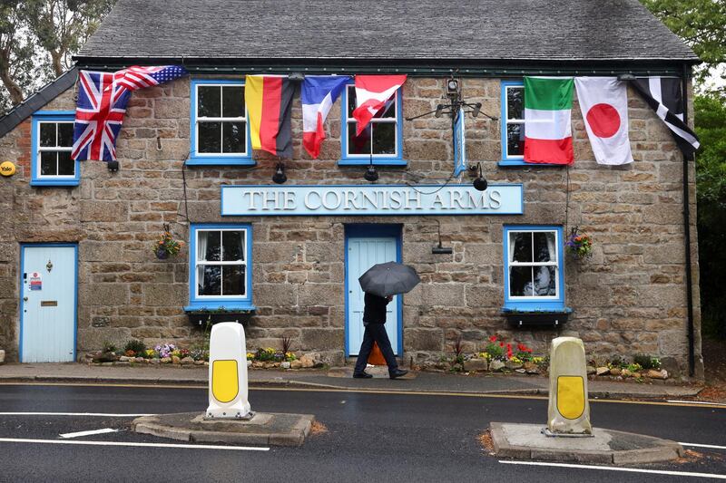 A person walks past The Cornish Arms pub as the G7 nations' flags flutter next to the Cornish flag. Reuters