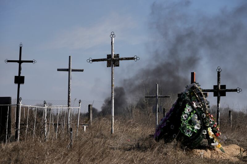 Smoke from shelling rises behind a wreath at a cemetery in Vasylkiv, Ukraine. AP