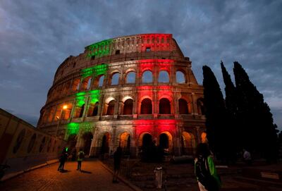 People walk in front of the Colosseum illuminated in the colors of the Italian flag on May 31, 2020, in Rome. The Colosseum reopens on June 1. / AFP / Tiziana FABI
