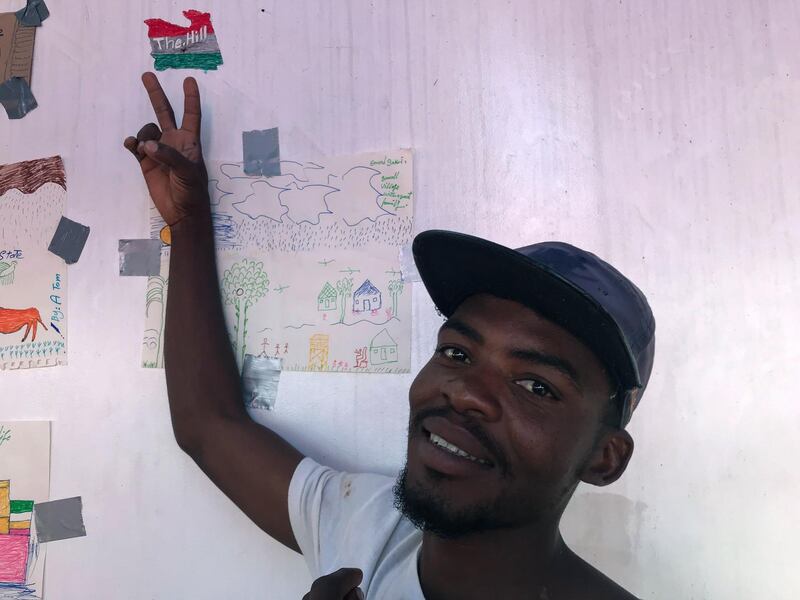 A rescued migrant called Allahaddin poses next to a map of Libya bearing the letters "Hill" (for "Hell") that he drew.