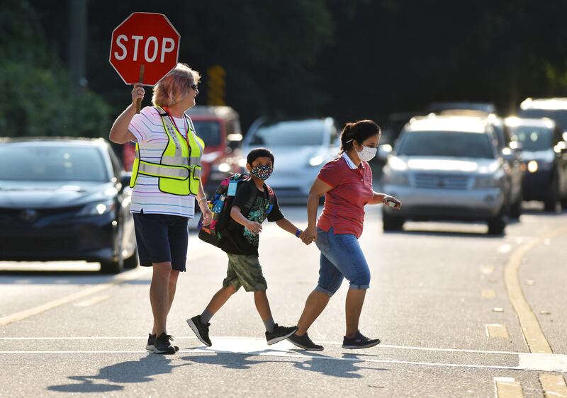 Crossing guard Kelly Linder helps a masked mother and son cross a road as they make their way to Loretto Elementary School on August 10, 2021, in Jacksonville, Florida, for the first day of the new school year. AP